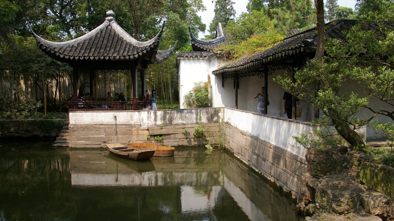 Pabellón de tejado curvo y muro encalado reflejados en el estanque de un jardín clásico de Suzhou