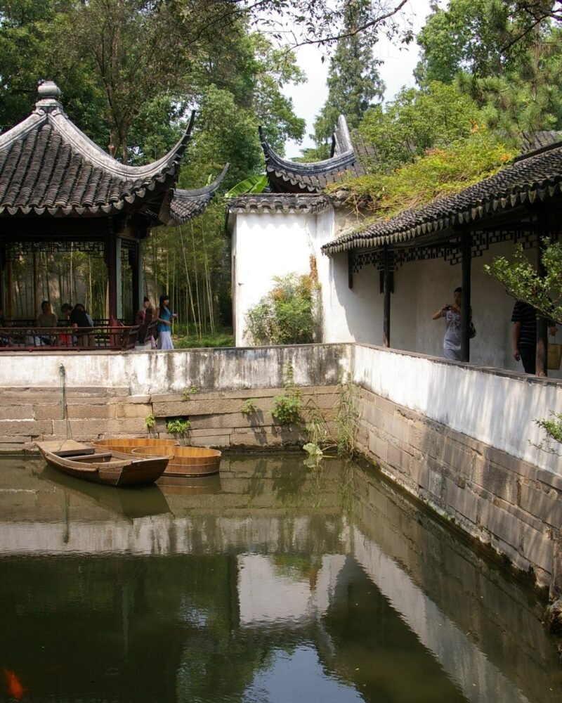 Pabellón de tejado curvo y muro encalado reflejados en el estanque de un jardín clásico de Suzhou